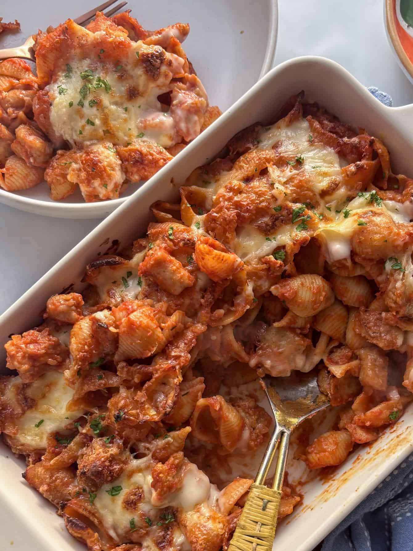 a creamy sausage pasta bake with a portion in a bowl on the side