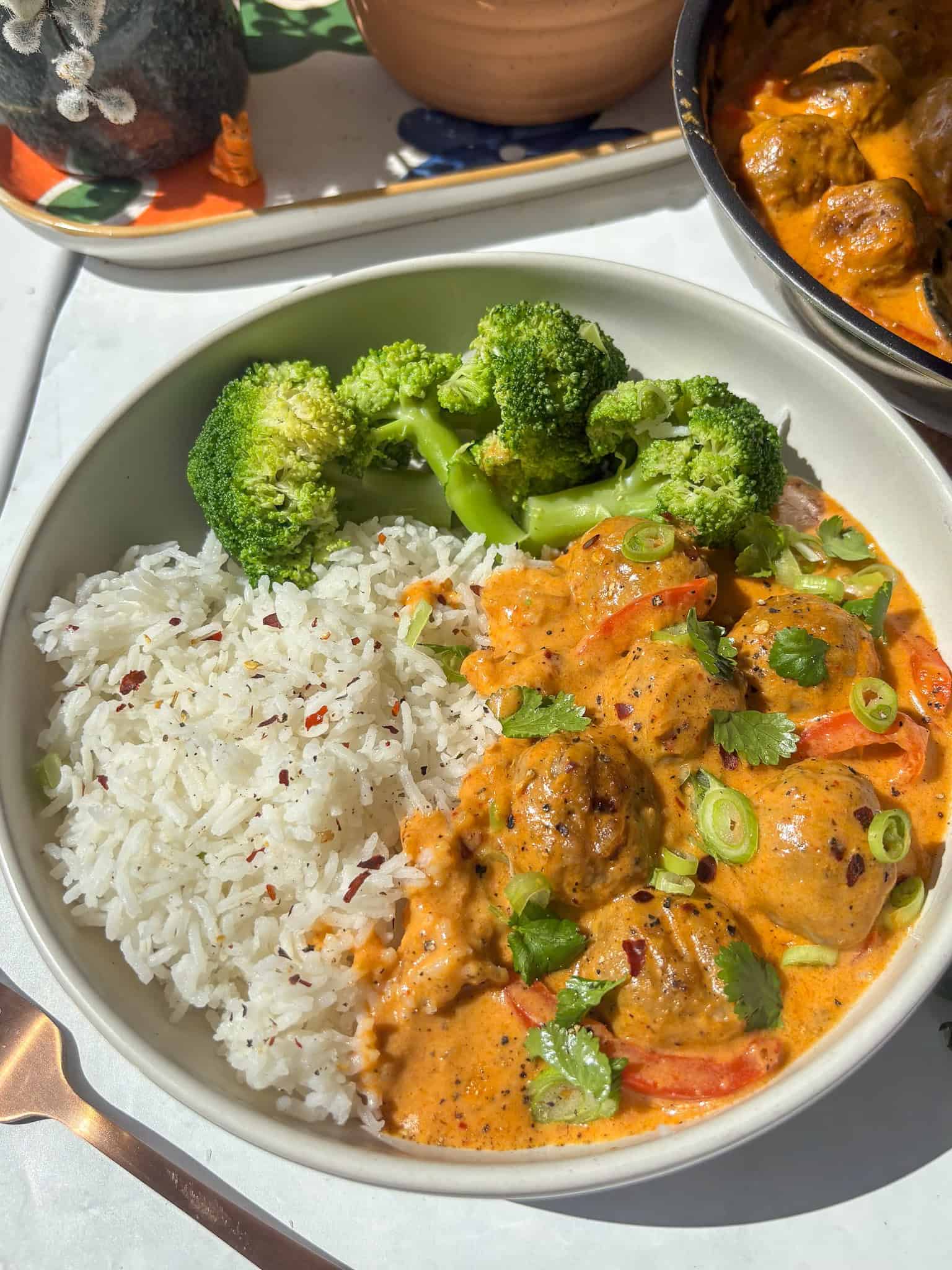creamy thai red meatball curry served with rice and broccoli - topped with red chili flakes, cilantrol, and sesame seeds