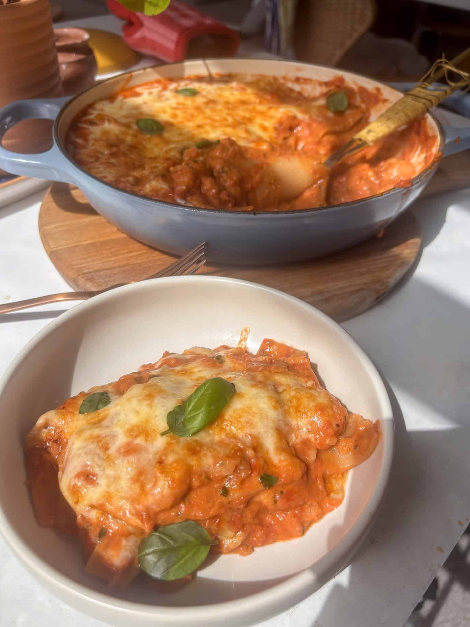 a bowl of butter bean lasagne topped with cheese and fresh basil leaves, with the remaining pan in the back