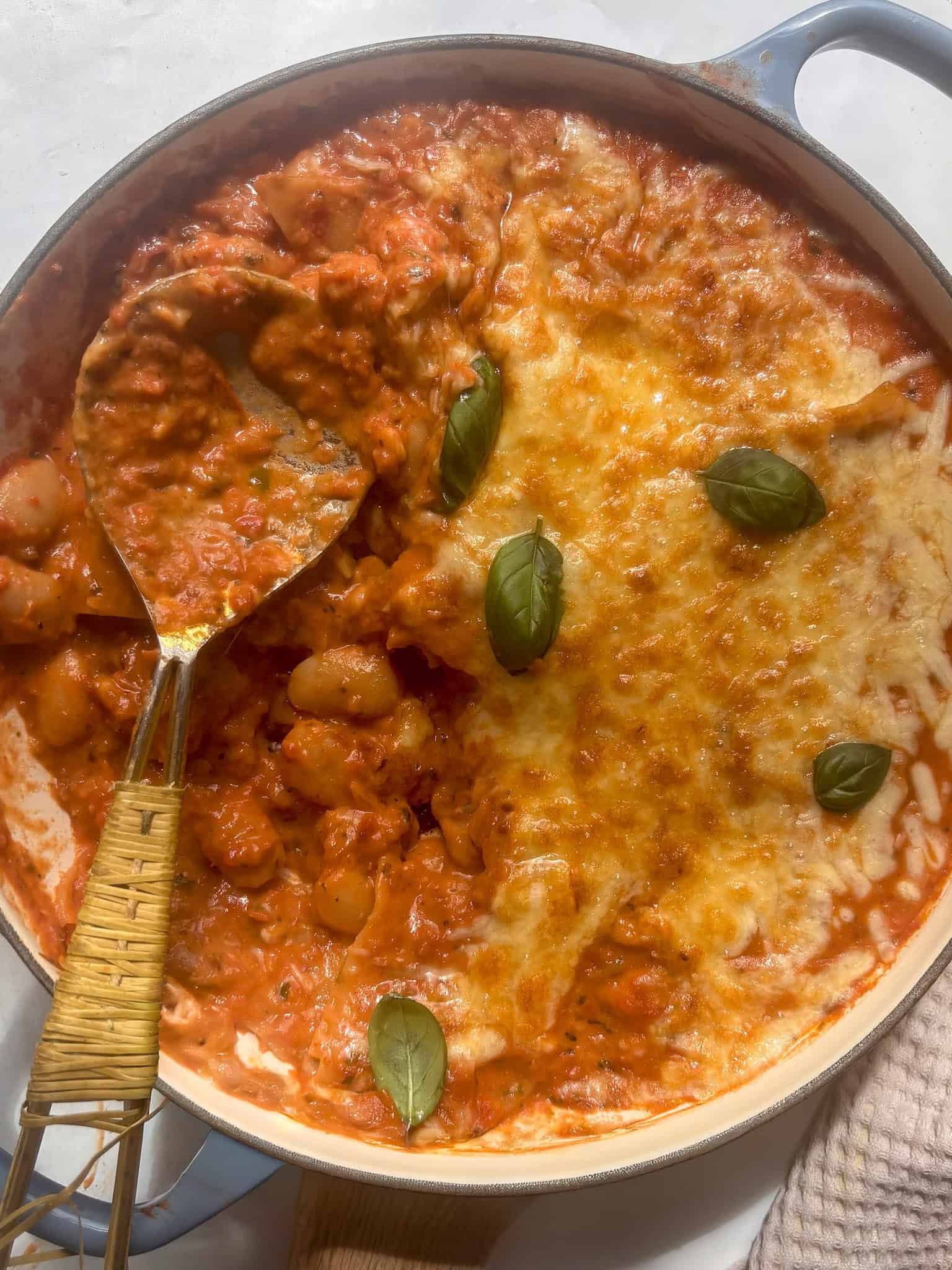 a pan of butter bean lasagne with a scoop taken out of it, topped with fresh basil leaves
