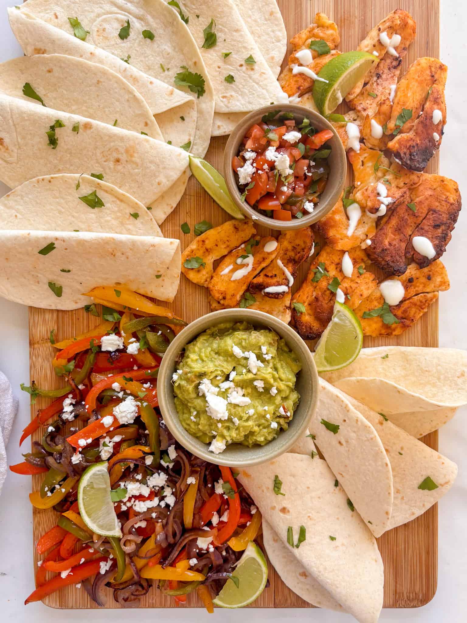 a chopping board laden with mexican halloumi and peppers, with tortilla wraps and bowls of dips arranged around it