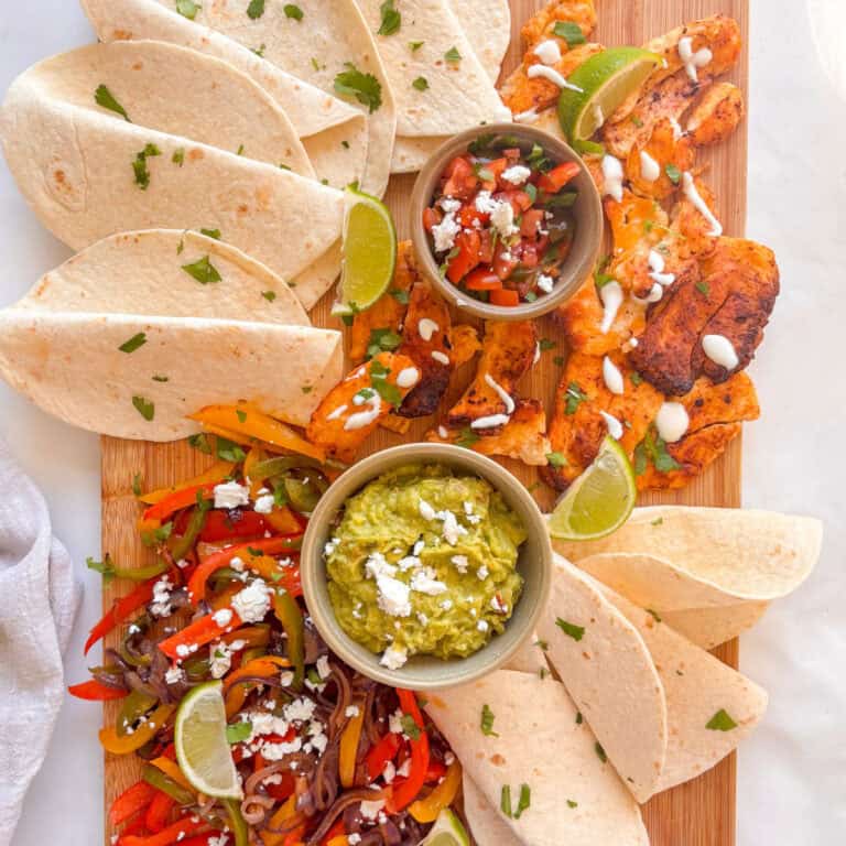 a tray of chipotle halloumi, fajita vegetables, tortilla wraps, a bowl of guacamole, and pico de gallo