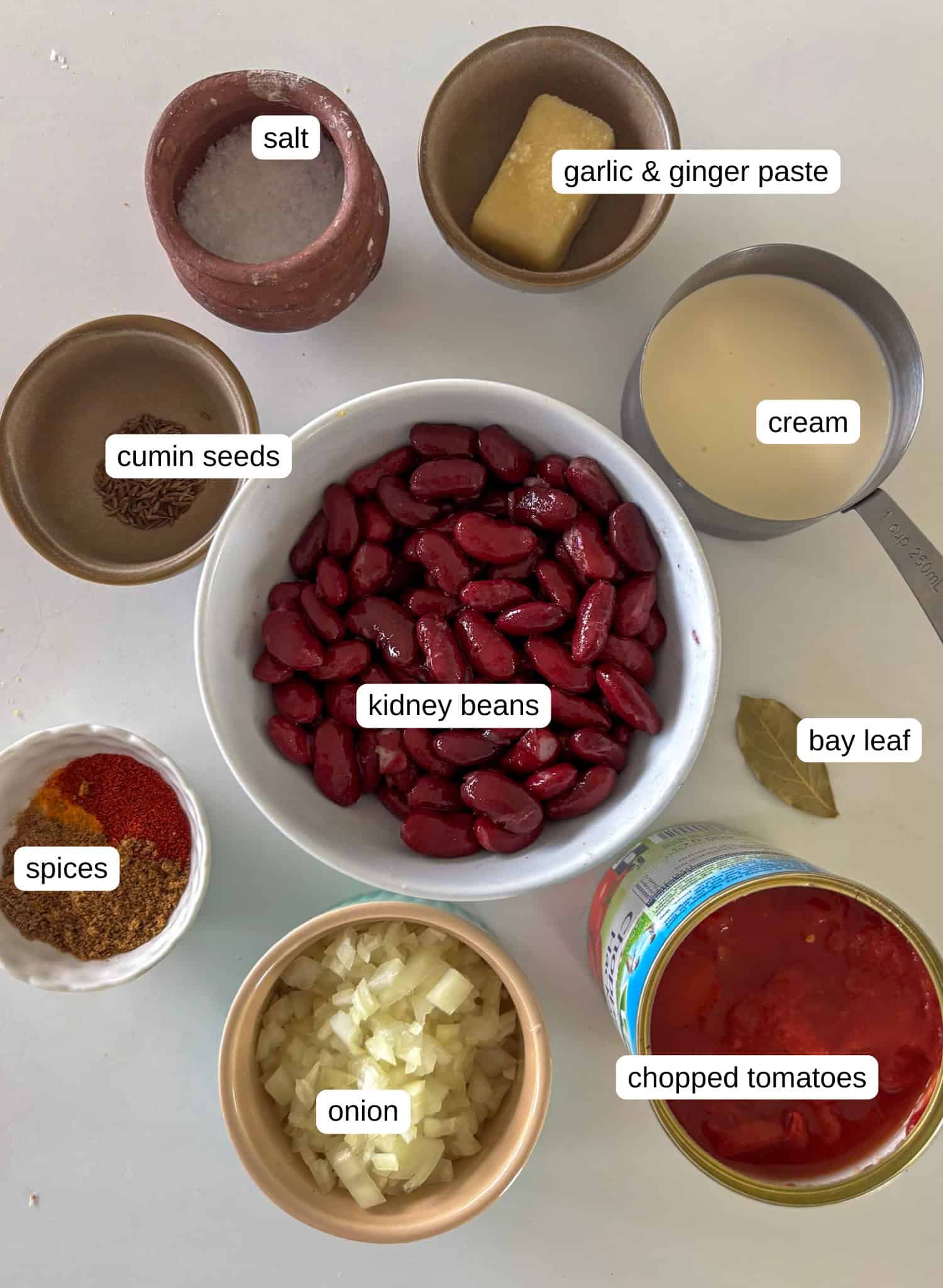 ingredients needed for rajma masala - salt, garlic and ginger paste, cumin seeds, cream, kidney beans, bay leaf, onion, chopped tomatoes, spices