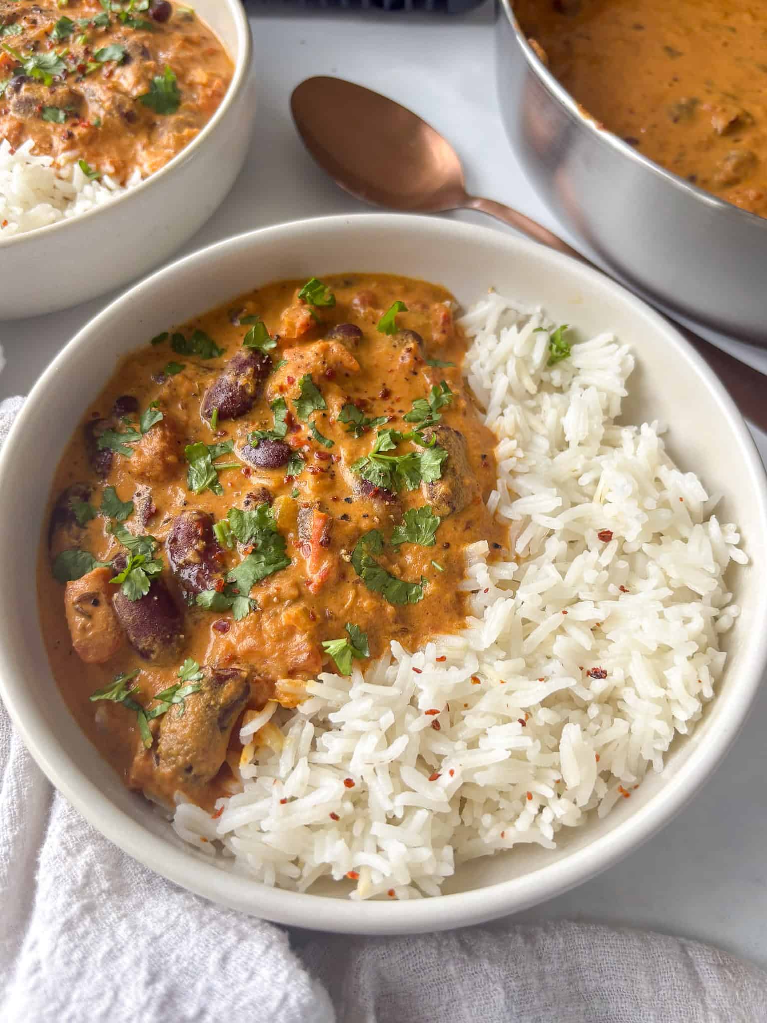 a bowl of rajma masala - kidney bean curry - served with white rice and topped with chili flakes and cilantro