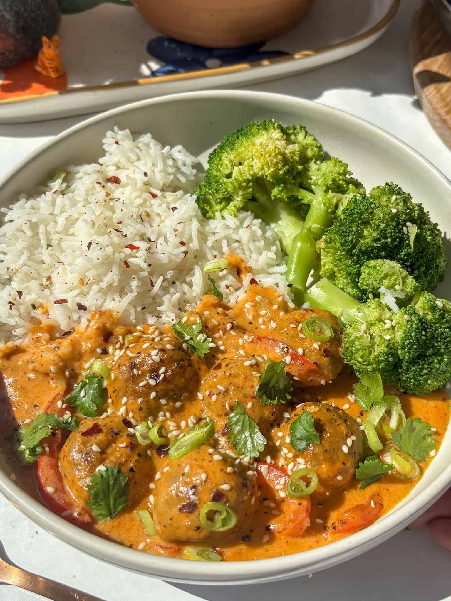 creamy thai red meatball curry served with rice and broccoli - topped with red chili flakes, cilantrol, and sesame seeds