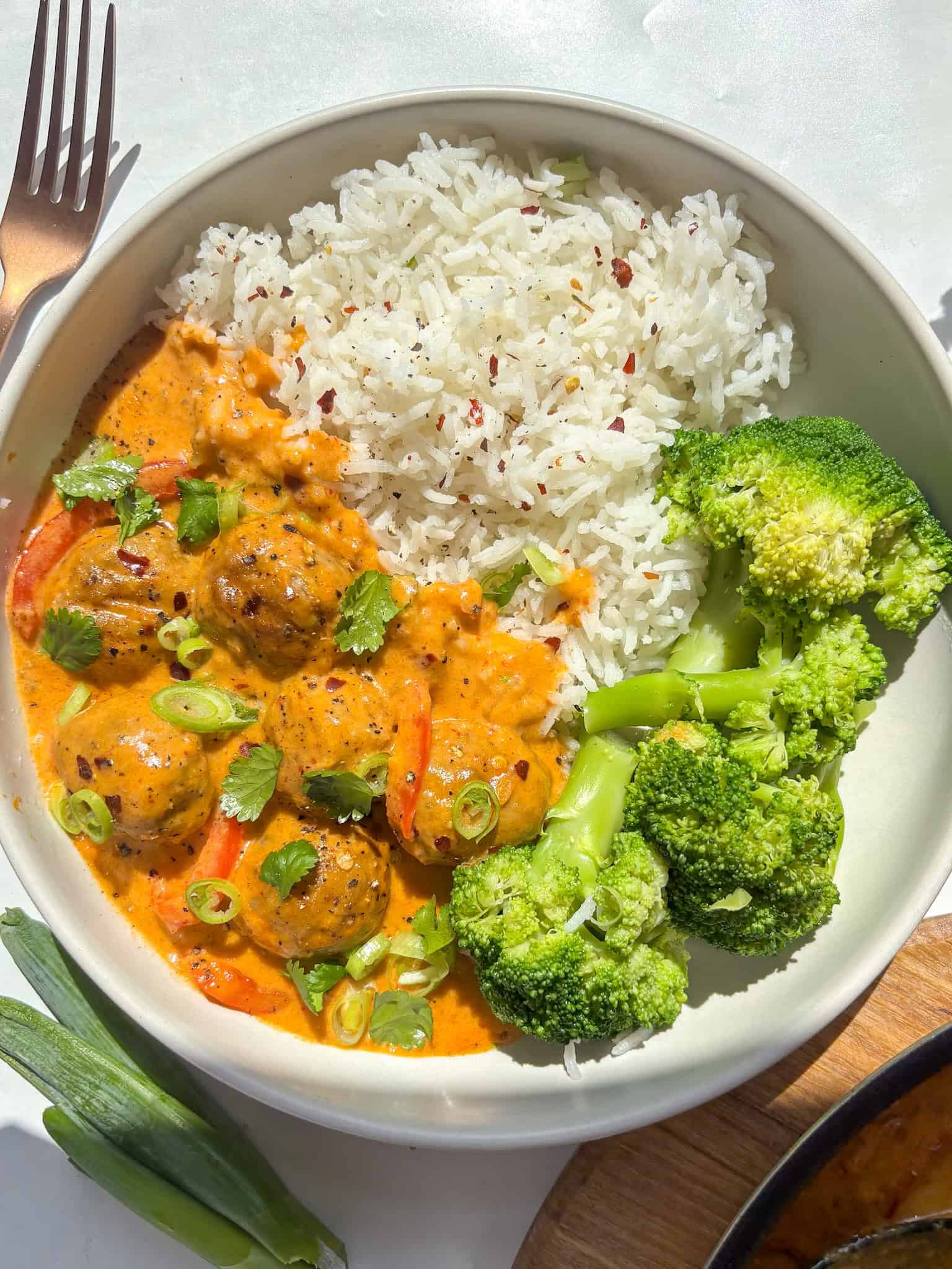 creamy thai red meatball curry served with rice and broccoli - topped with red chili flakes, cilantrol, and sesame seeds