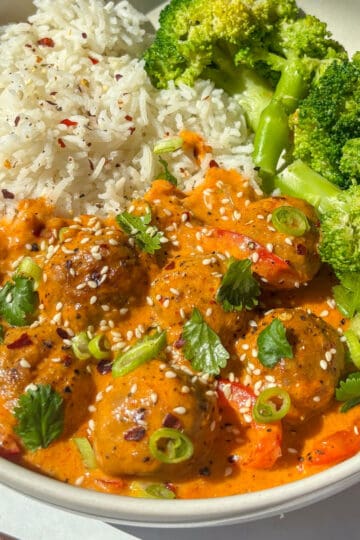creamy thai red meatball curry served with rice and broccoli - topped with red chili flakes, cilantrol, and sesame seeds