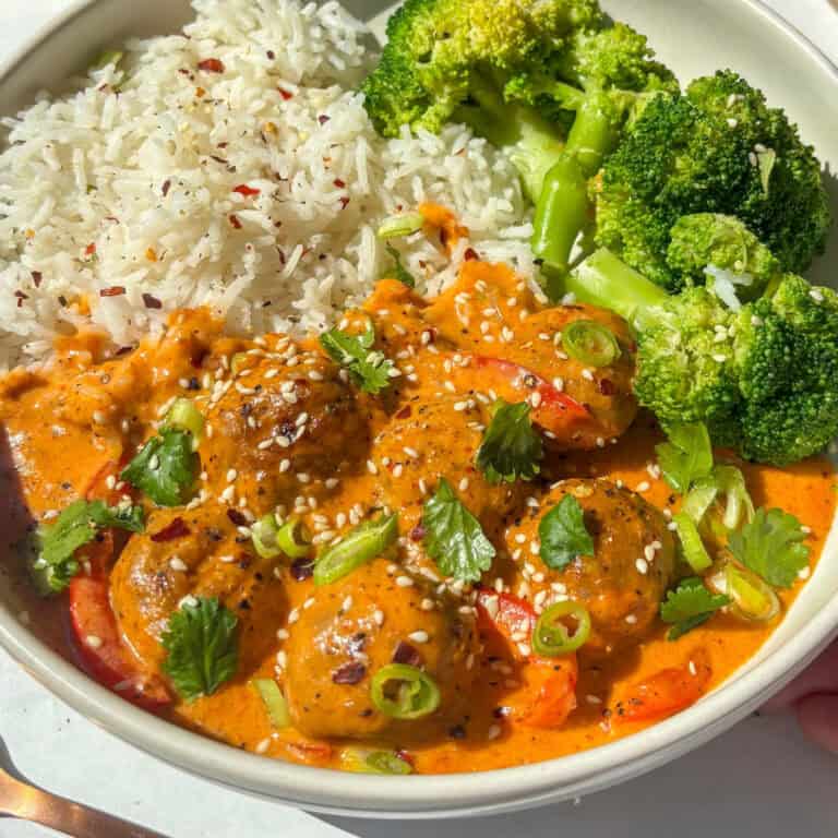 creamy thai red meatball curry served with rice and broccoli - topped with red chili flakes, cilantrol, and sesame seeds