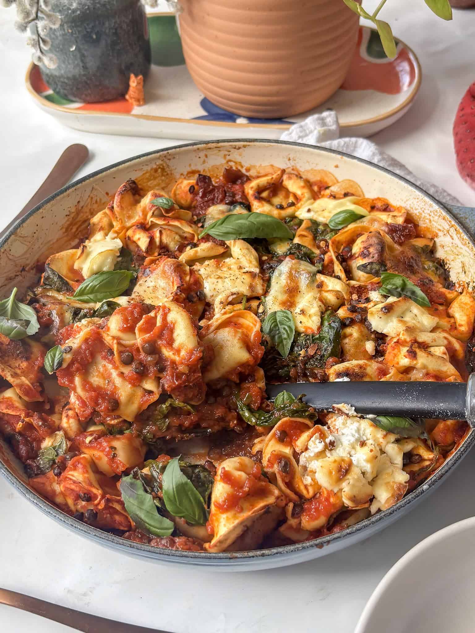 a casserole pan of baked tortellini topped with mozzarella and basil