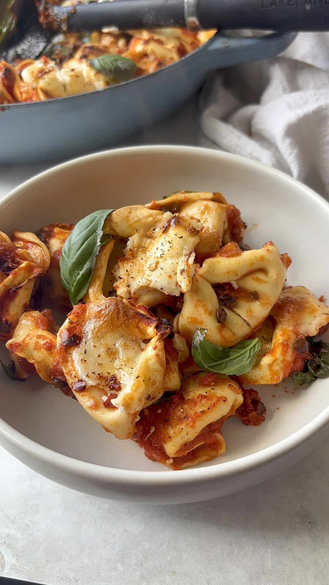 a bowl of baked tortellini topped with mozzarella and basil