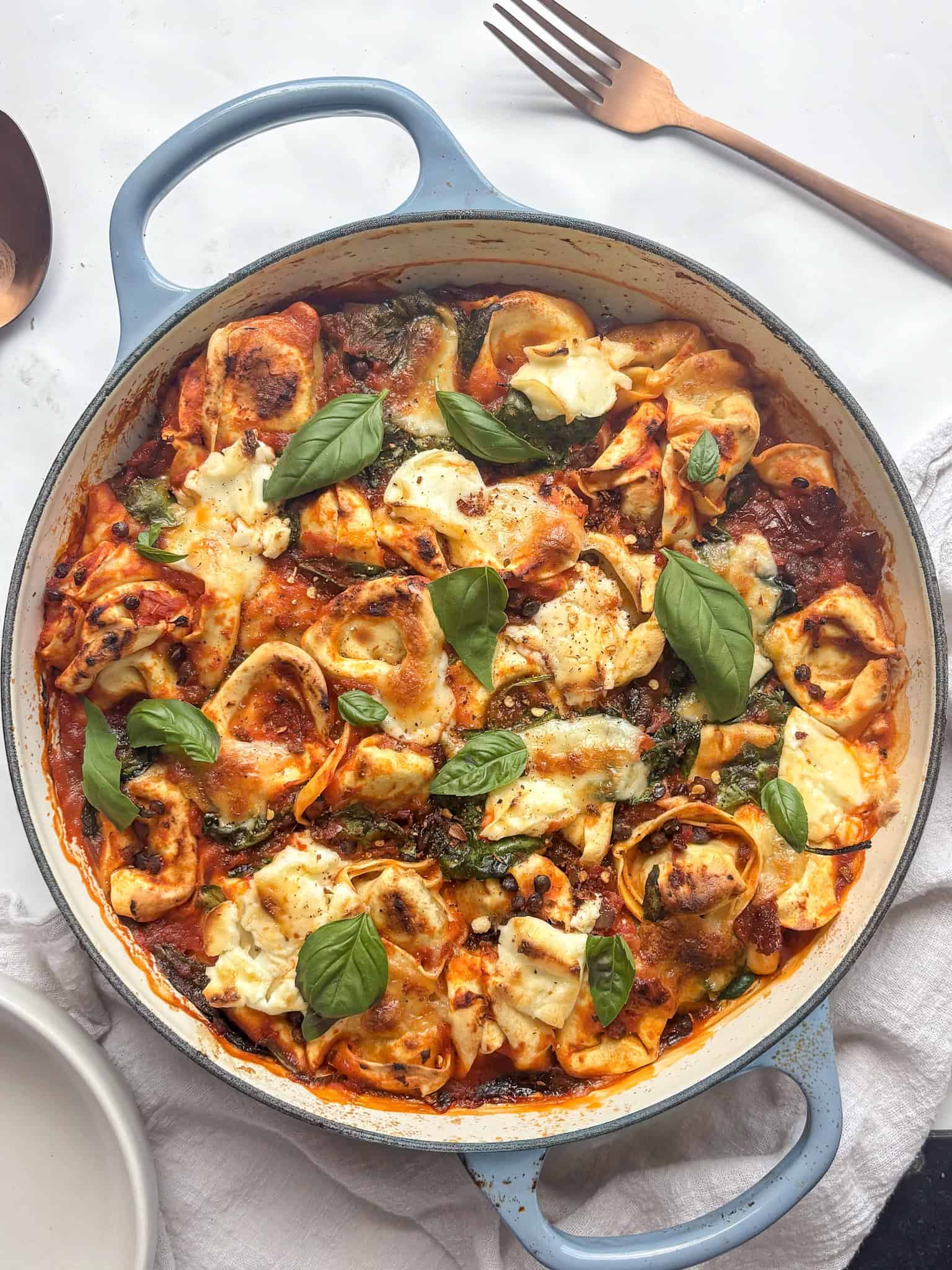 a casserole pan of baked tortellini topped with mozzarella and basil