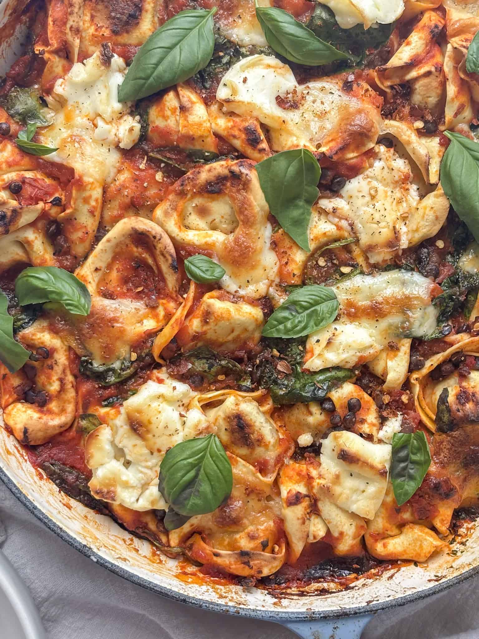 a casserole pan of baked tortellini topped with mozzarella and basil