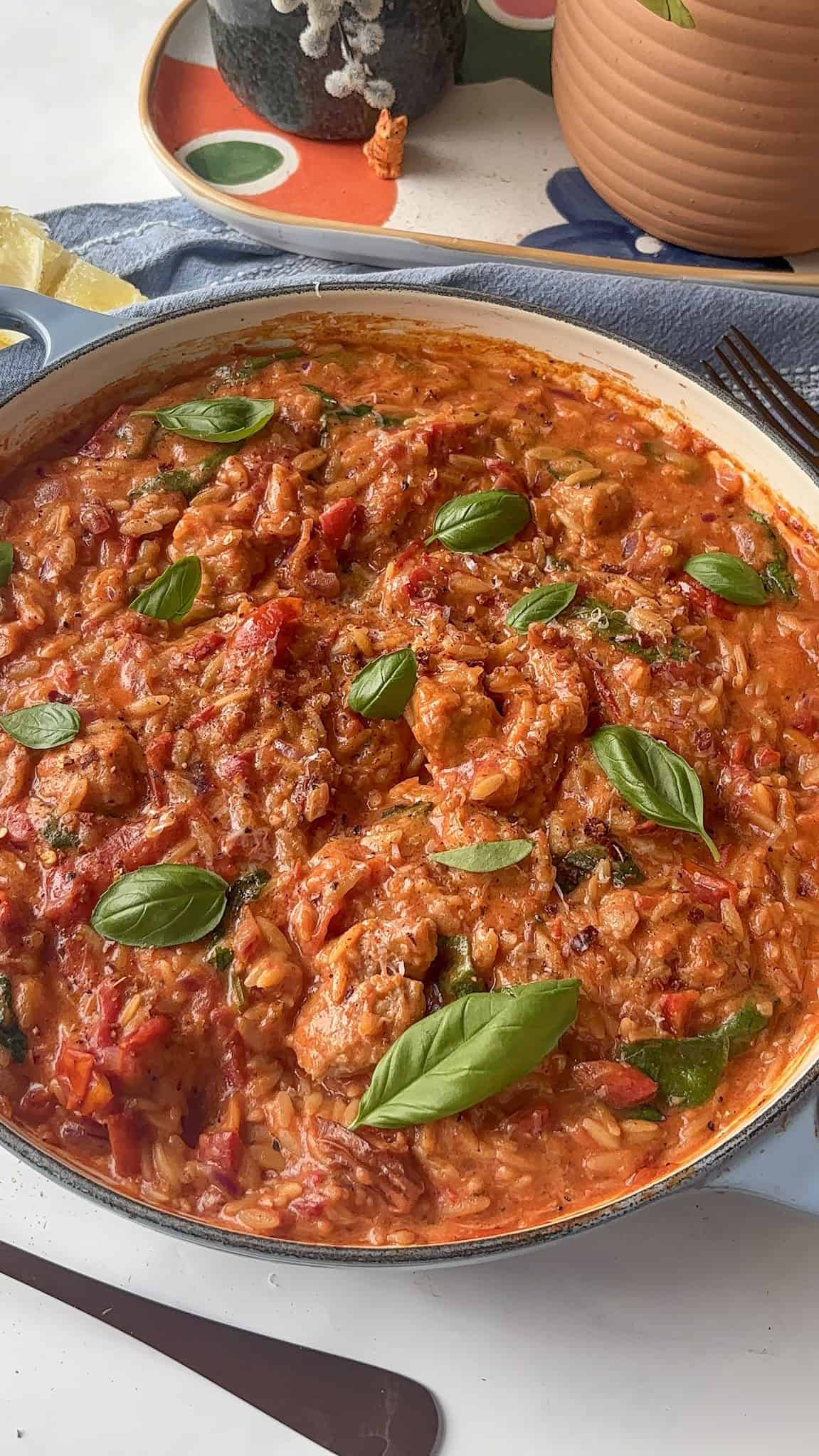 a close up shot of cheesy cajun sausage orzo topped with fresh basil leaves
