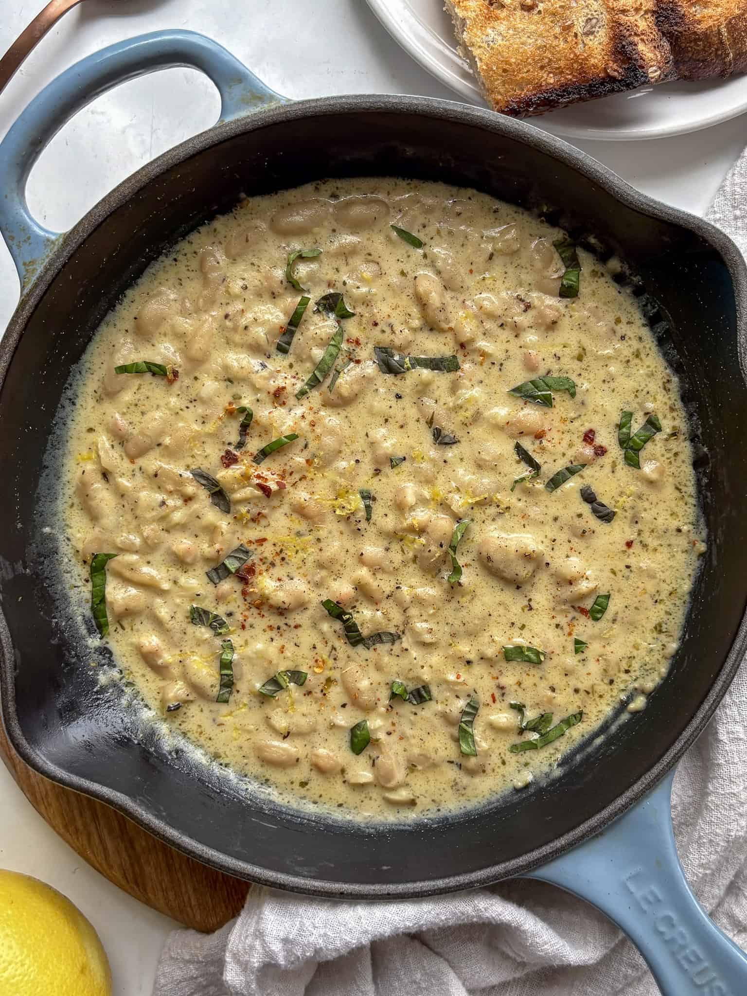 a cast iron skillet with garlic parmesan beand topped with basil and lemon zest