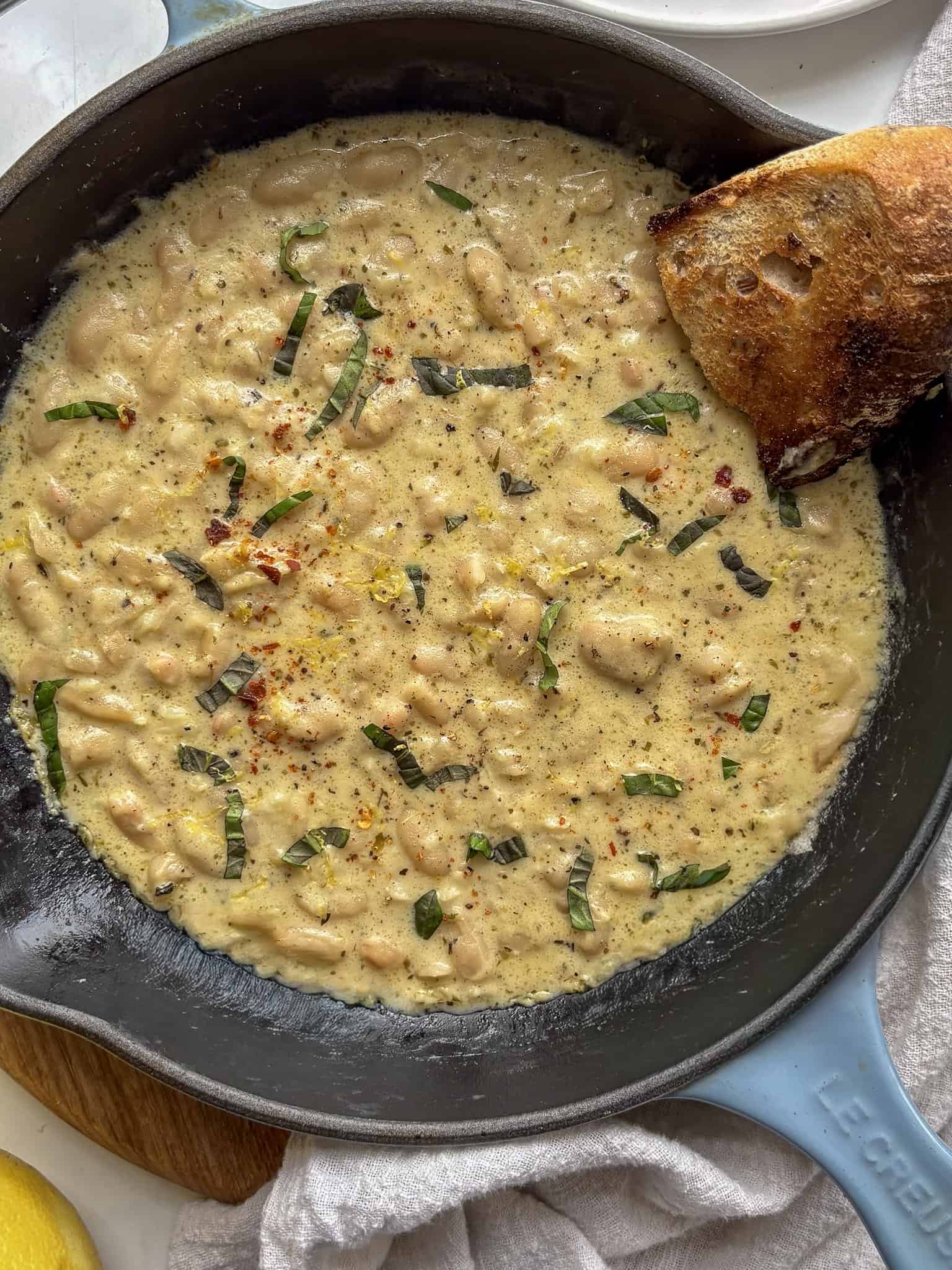 a cast iron skillet with garlic parmesan beand topped with basil and lemon zest