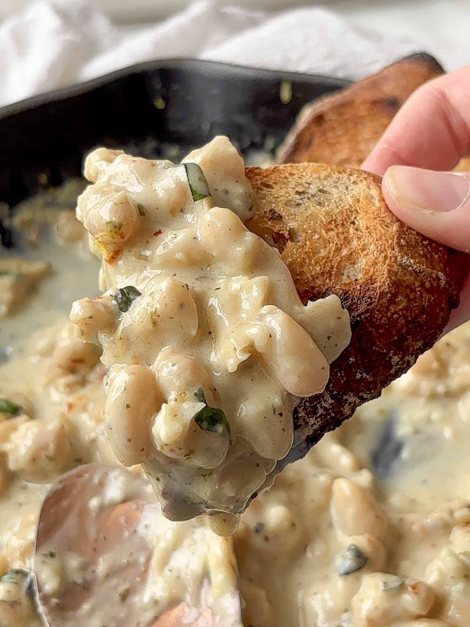 a portion of garlic parmesan beans scooped up by crusty bread