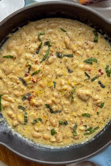 a cast iron skillet with garlic parmesan beand topped with basil and lemon zest