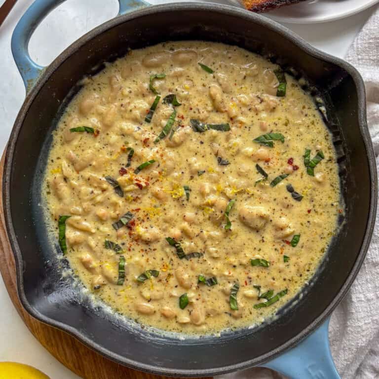 a cast iron skillet with garlic parmesan beand topped with basil and lemon zest