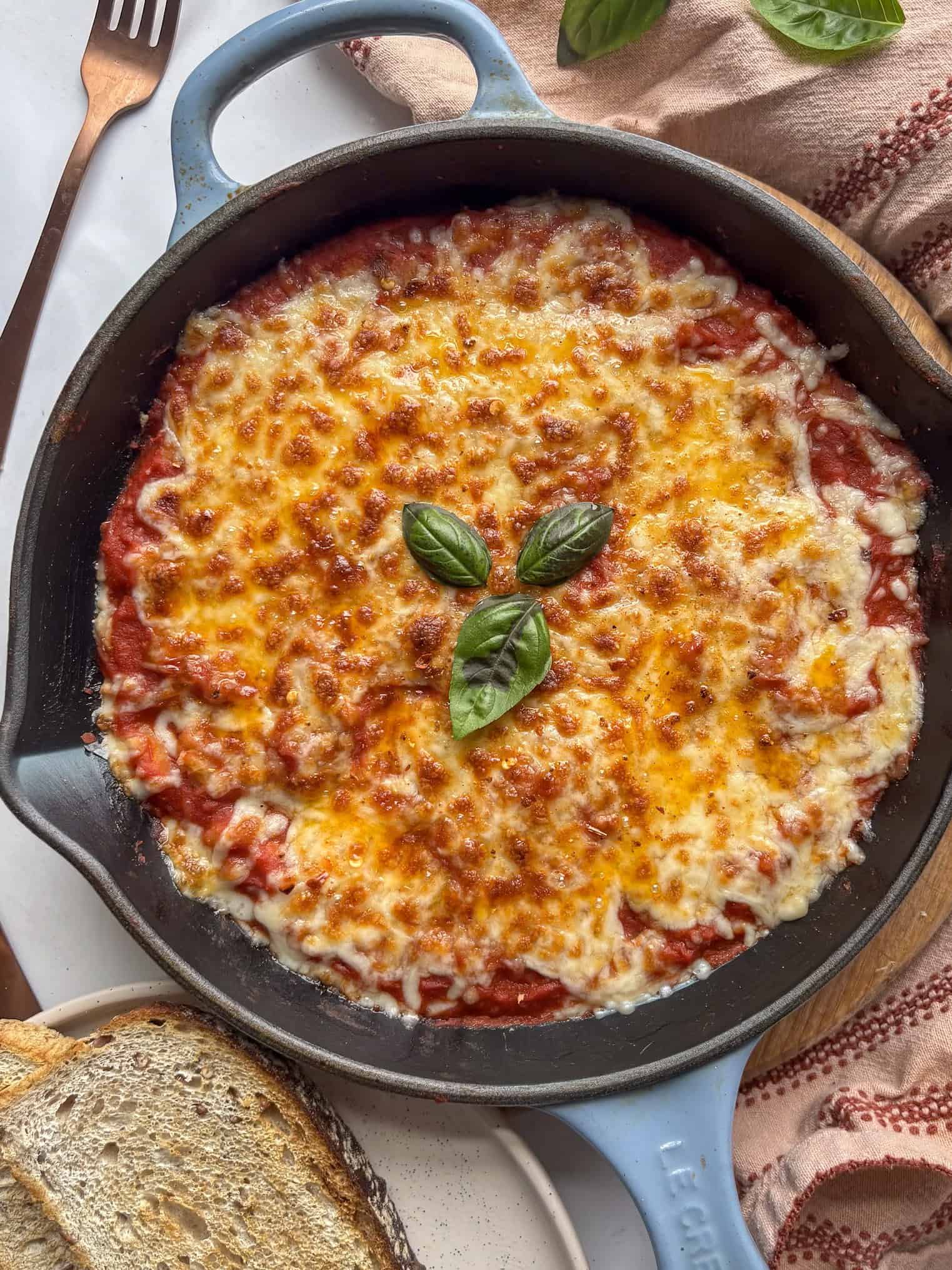 a cast iron skillet of pizza beans - tomato white beans topped with a golden cheesy layer and fresh basil leaves