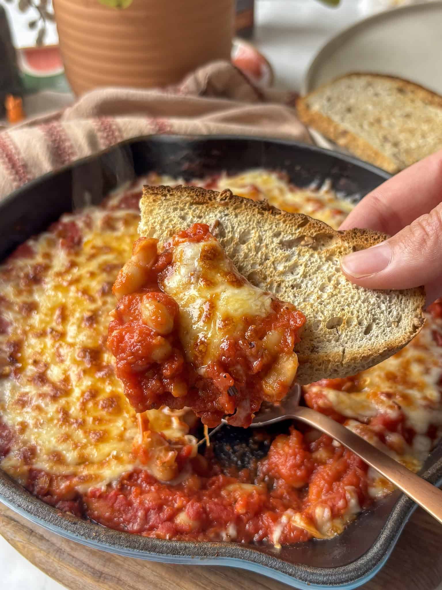 pizza beans in a cast iron skillet, a slice of garlic bread having taken a scoop of the beans out of it.