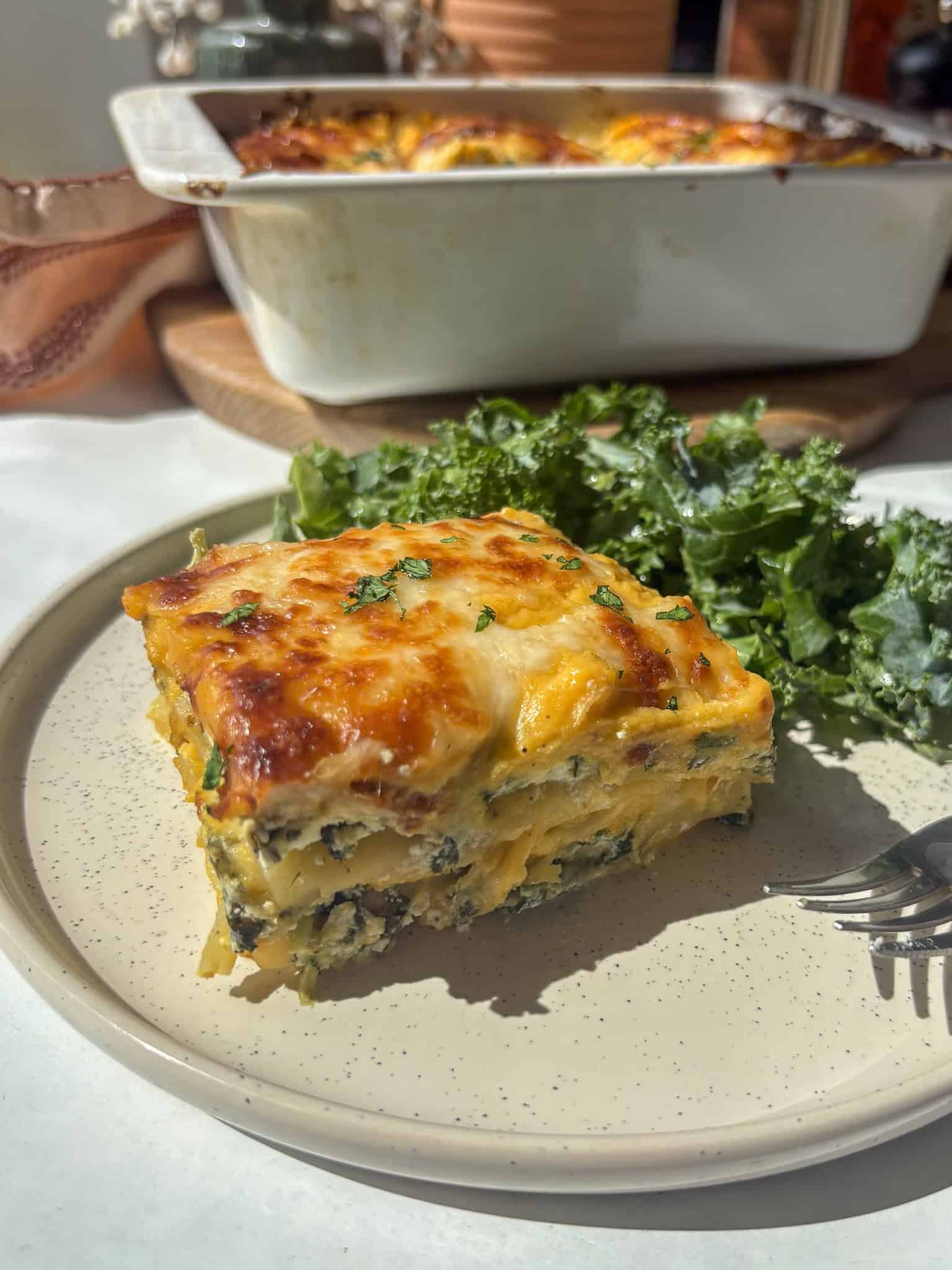 a portion of butternut squash and spinach lasagne on a plate with a kale salad