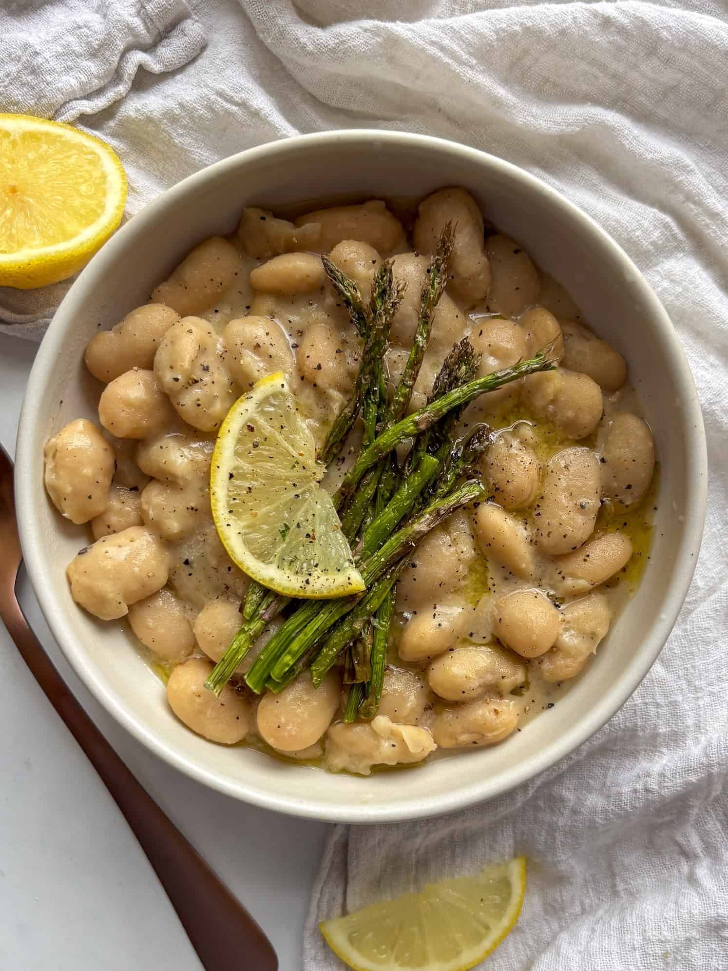 a bowl of creamy cacio e pepe beans topped with grilled asparagus and lemon