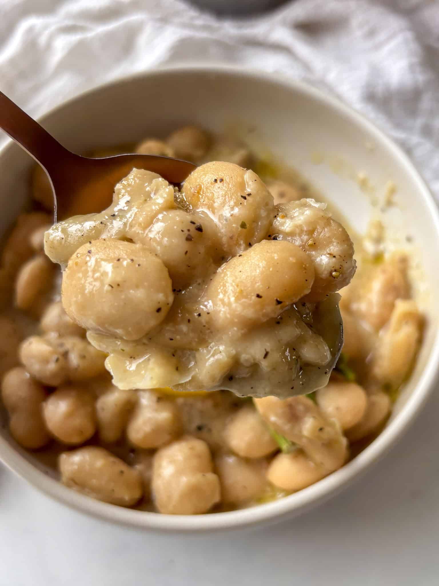 a bowl of creamy cacio e pepe beans topped with grilled asparagus and lemon