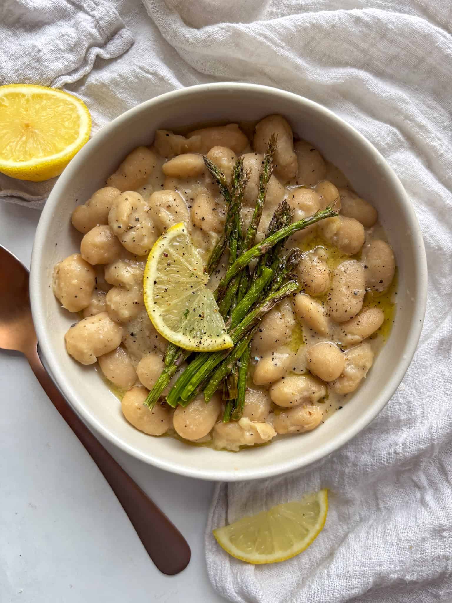 a bowl of creamy cacio e pepe beans topped with grilled asparagus and lemon