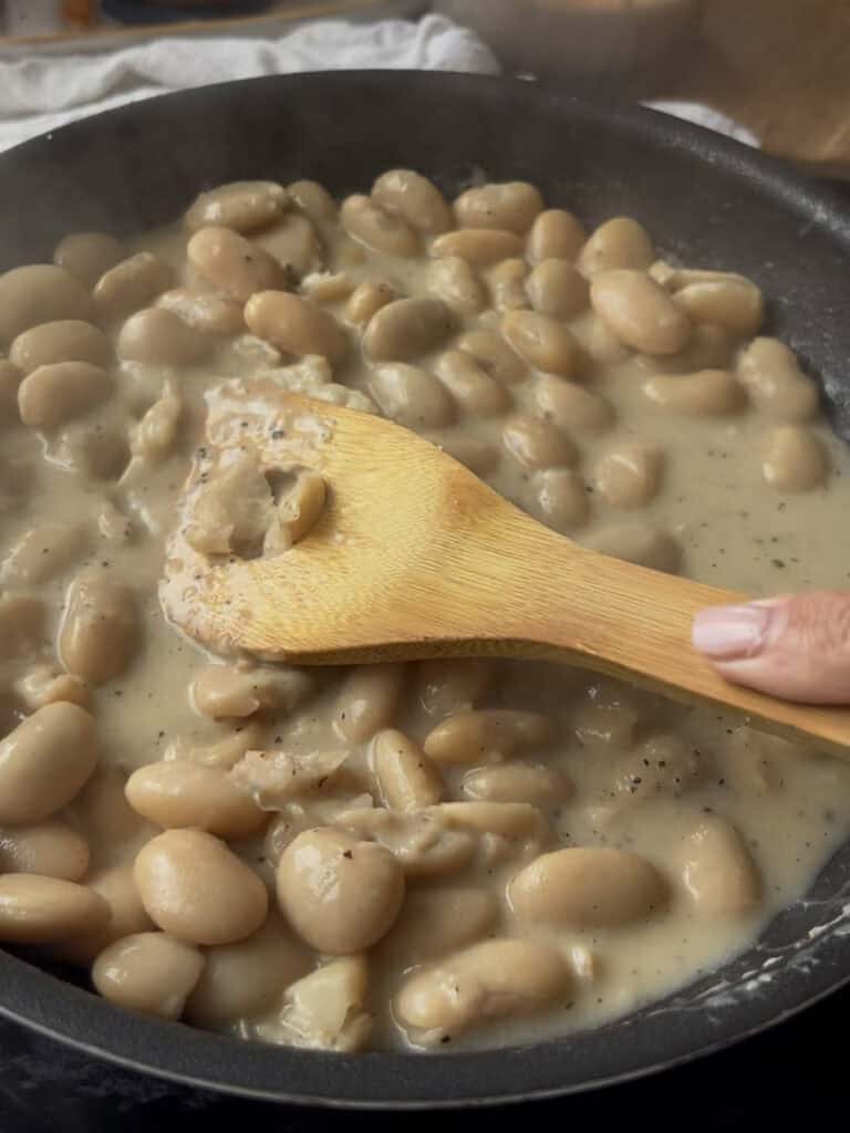 some of the butter beans in the cacio e pepe dish are mashed with the back of a wooden spoon for a creamier texture