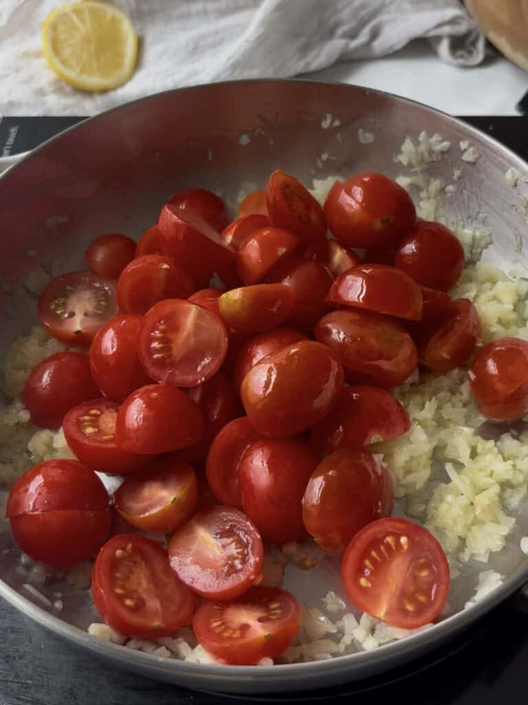 halved cherry tomatoes are added to a pan with sauted diced onion and garlic in olive oil