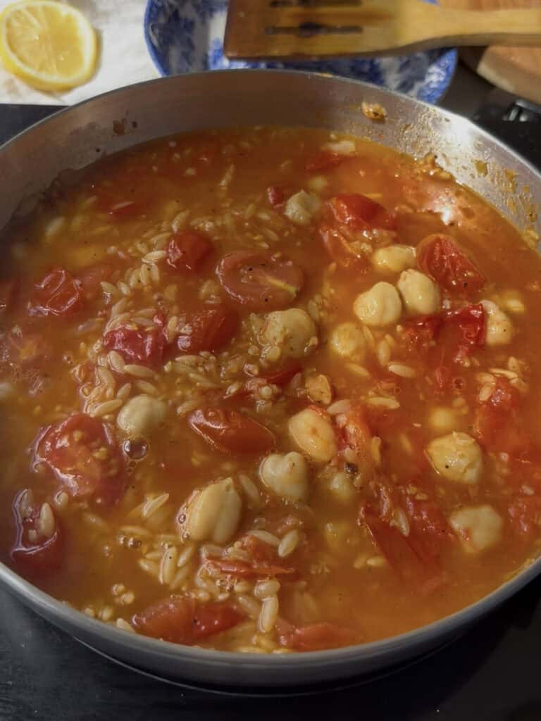 orzo, chickpeas, and cherry tomatoes simmer in vegetable stock to cook the orzo