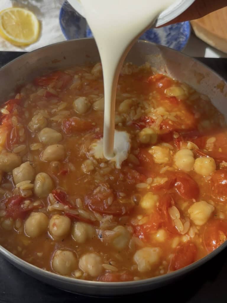 a dash of cream is poured into the chickpea and cherry tomato orzo sauce