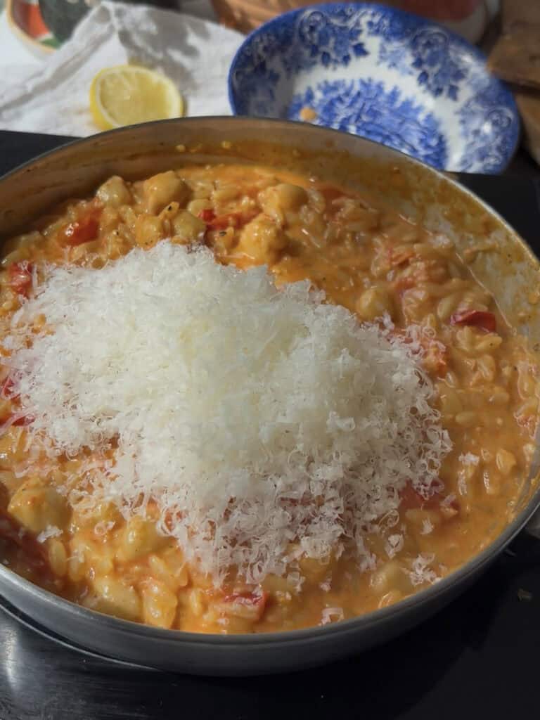 finely grated cheese is added to the cherry tomato orzo sauce, ready to be stirred in