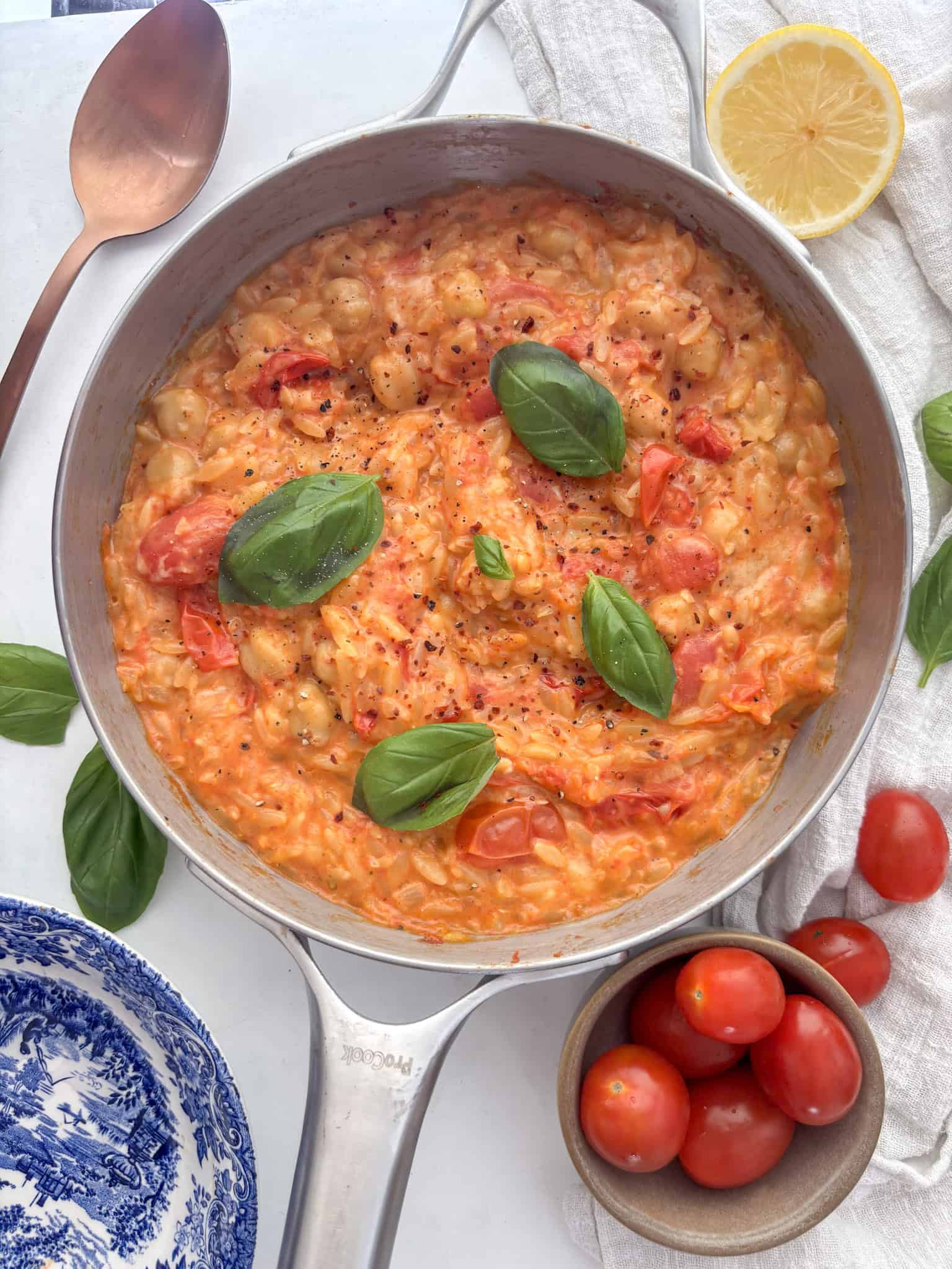 a pan of cherry tomato orzo, with fresh basil, chickpeas and a scattering of chili flakes on top