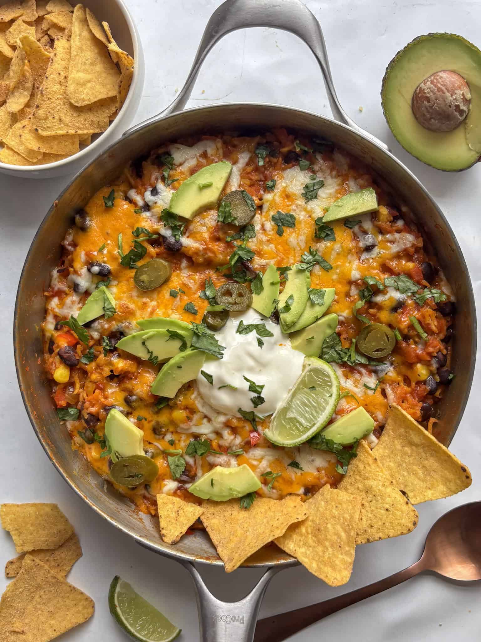 enchilada rice casserole with halloumi and black beans, topped with melted cheese, tortilla chips, jalapenos, and avocado