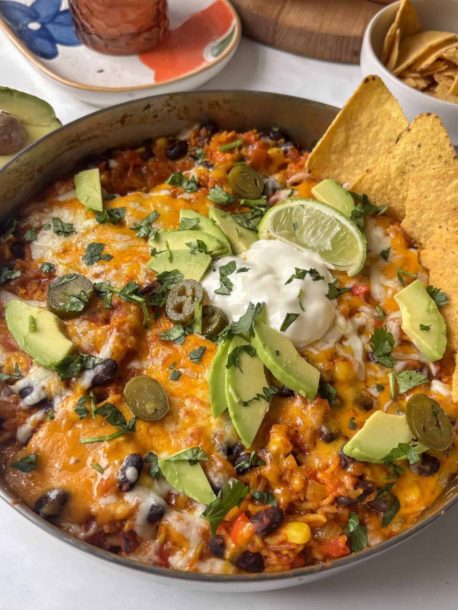 enchilada rice casserole with halloumi and black beans, topped with melted cheese, tortilla chips, jalapenos, and avocado
