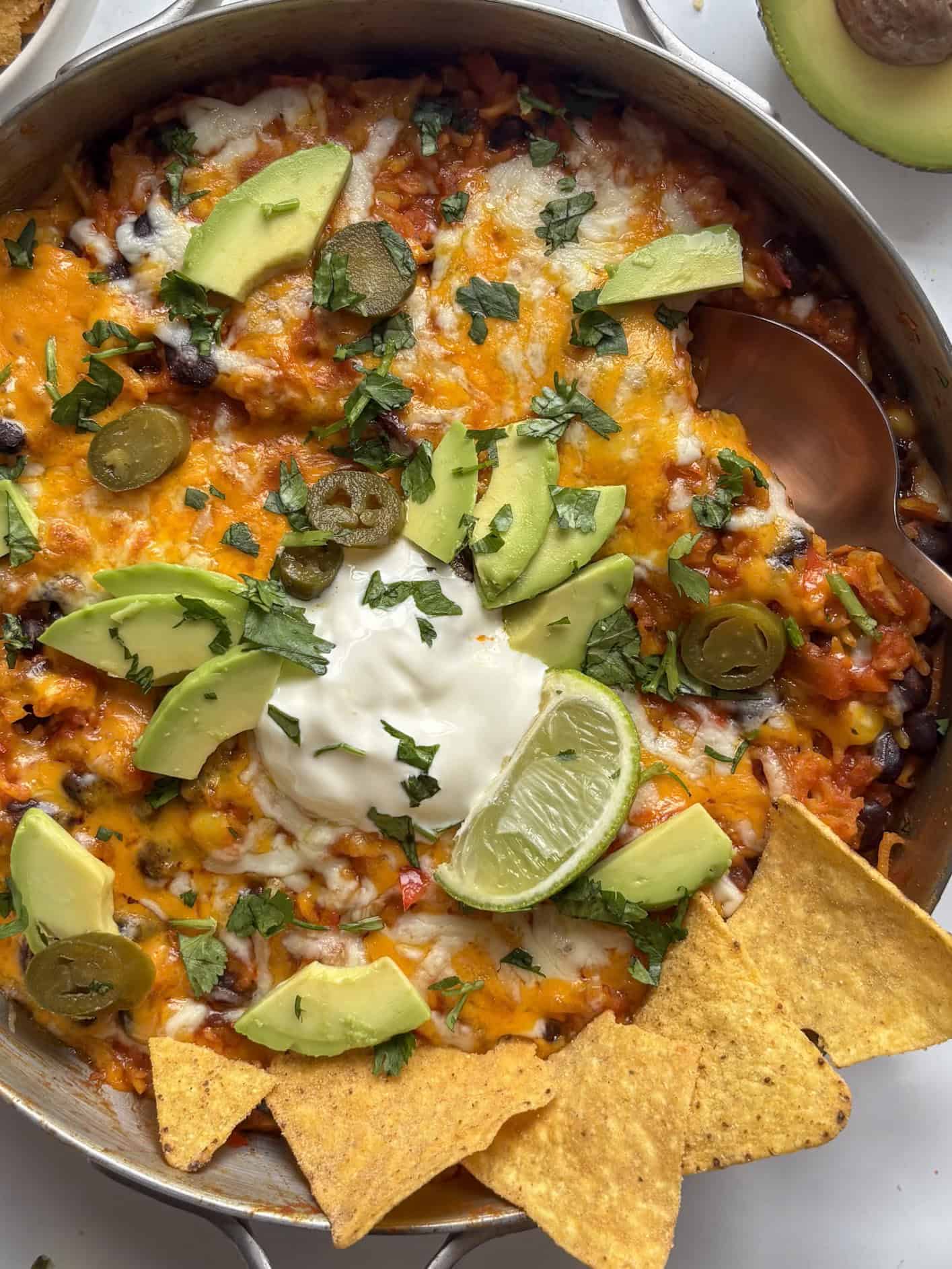 enchilada rice casserole with halloumi and black beans, topped with melted cheese, tortilla chips, jalapenos, and avocado