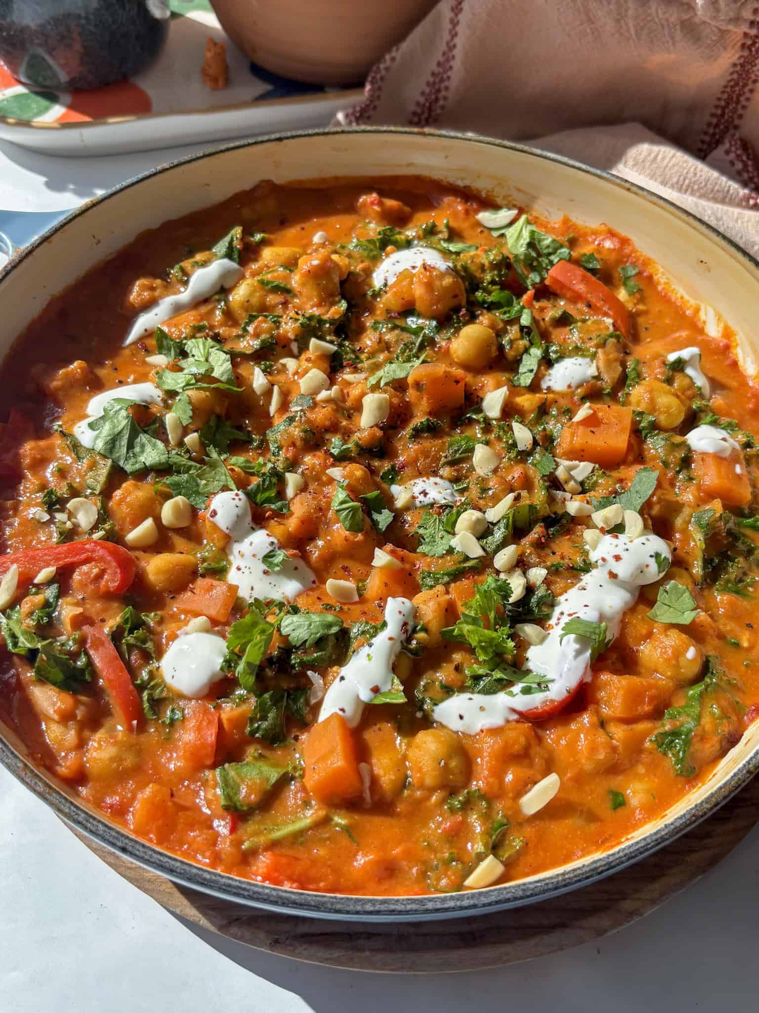 a casserole pan of creamy chickpea peanut stew topped with natural yoghurt, nuts, and coriander