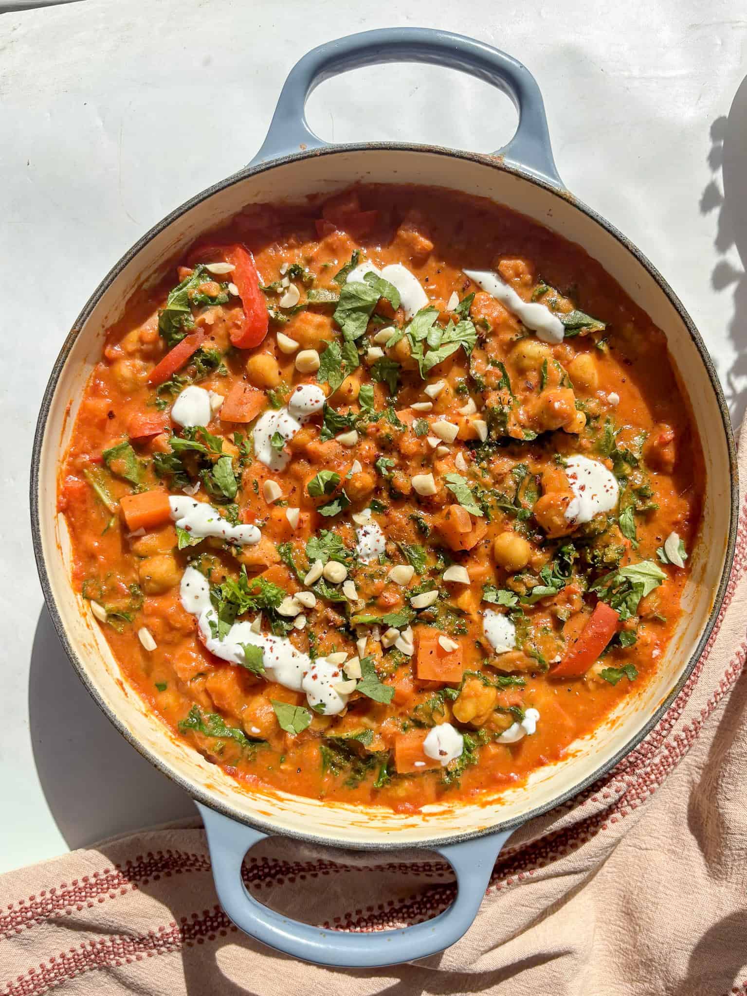 the casserole pan of creamy peanut chickpea stew topped with natural yogurt, chopped nuts, and coriander