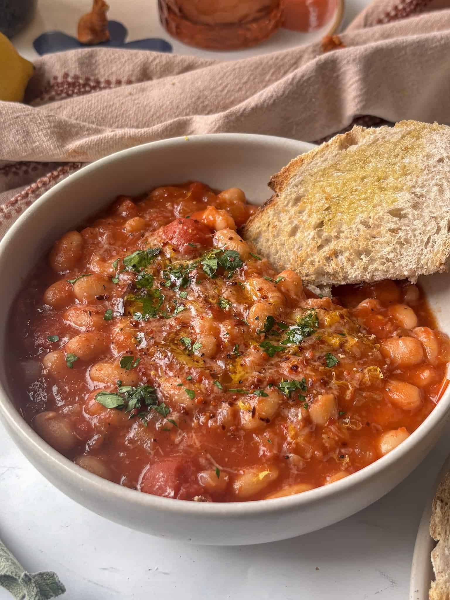 white bean stew in a bowl with cherry tomatoes and Pecorino cheese, with a slice of sourdough bread on the side